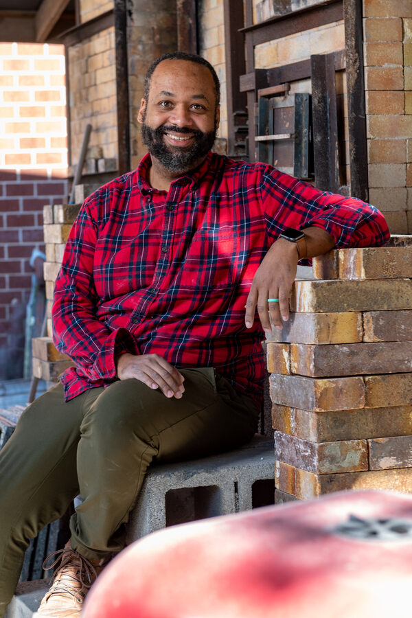 Scott Wayman in plaid shirt sitting in ceramic studio.